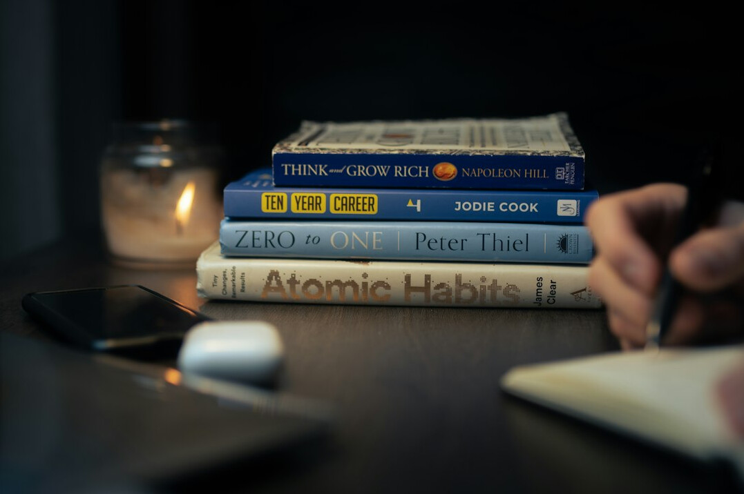 Hands writing in a notebook next to a stack of books